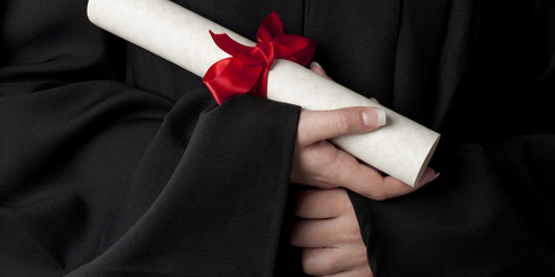 Ein gerolltes Dokument mit roter Schleife wird von Händen gehalten. Die Person trägt eine schwarze Robe.