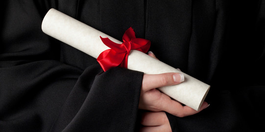 A rolled document with red bow is held by hands. 