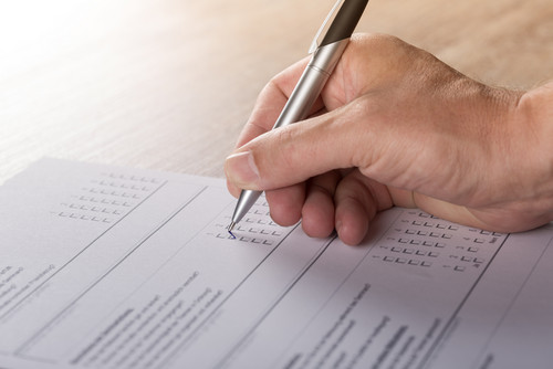 A hand holding a pen fills out a survey questionnaire.