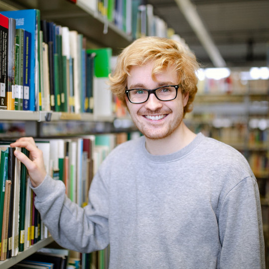 Student stands between two bookshelves.